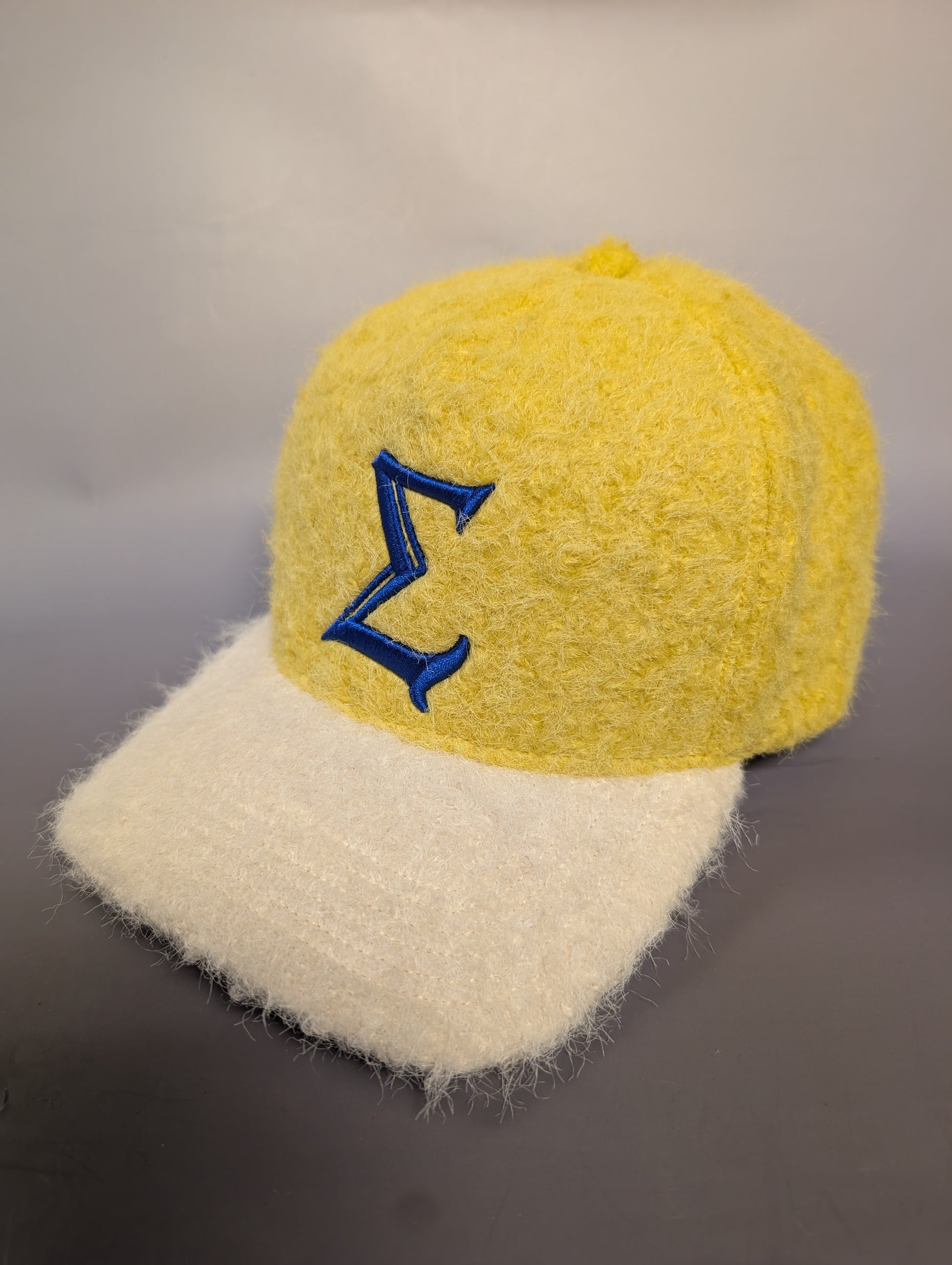 Yellow and cream fuzzy cap with a blue sigma embroidered