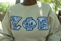 Person wearing a light-colored sweatshirt with 'Zeta Phi Beta' letters.