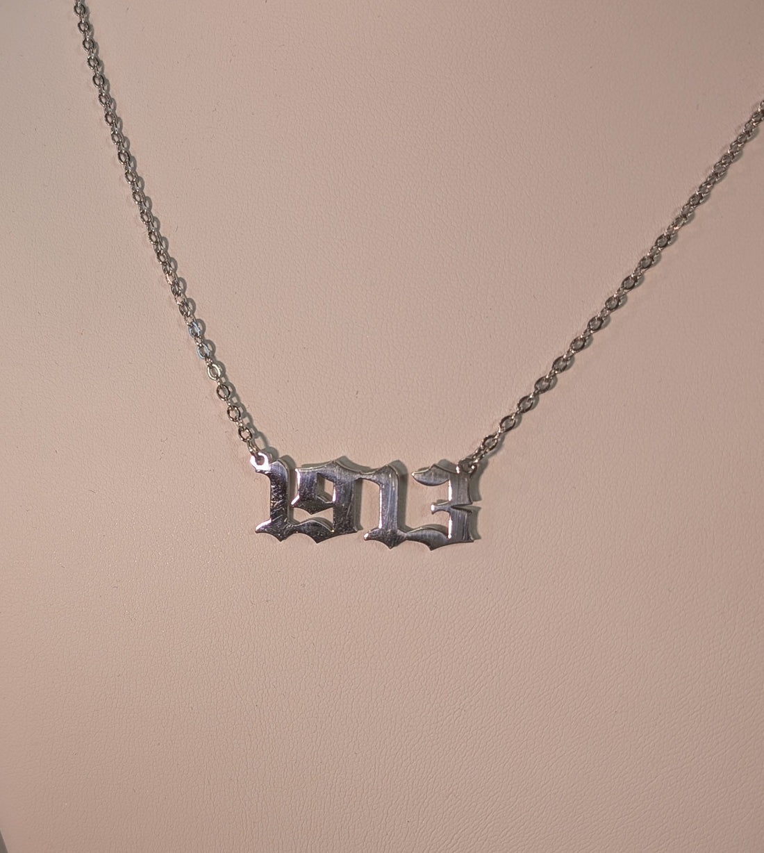 Silver necklace with a '1913' pendant on a beige background