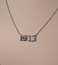 Silver necklace with a '1913' pendant on a beige background