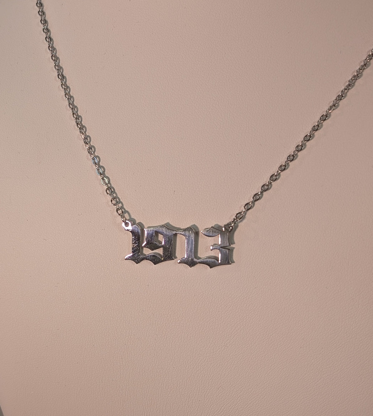 Silver necklace with a '1913' pendant on a beige background