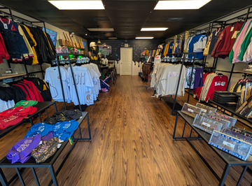 Clothing store interior with racks of shirts and jackets on a wooden floor.
