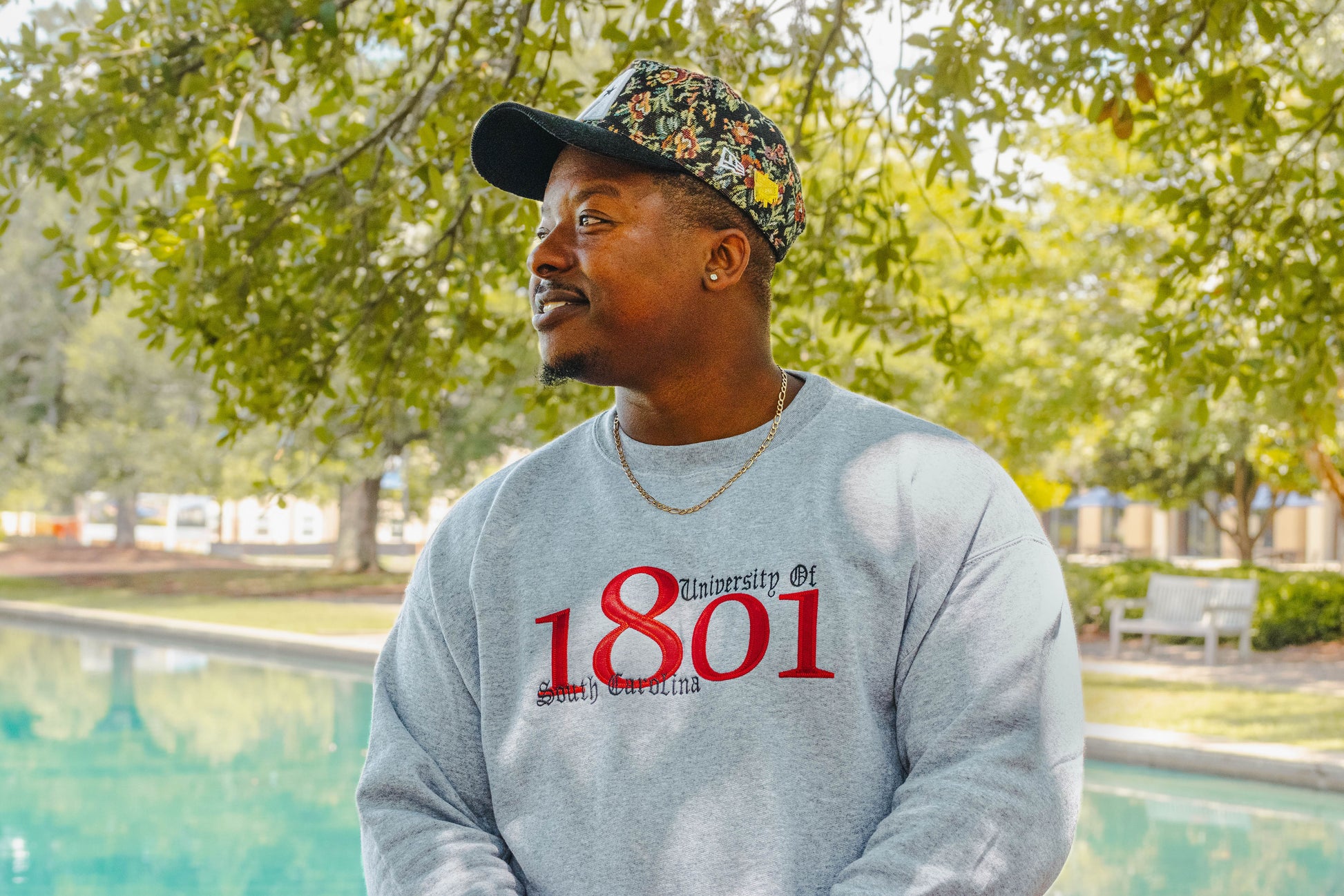 Person wearing a gray sweatshirt with 'University of 1801' text, standing outdoors near a pool.