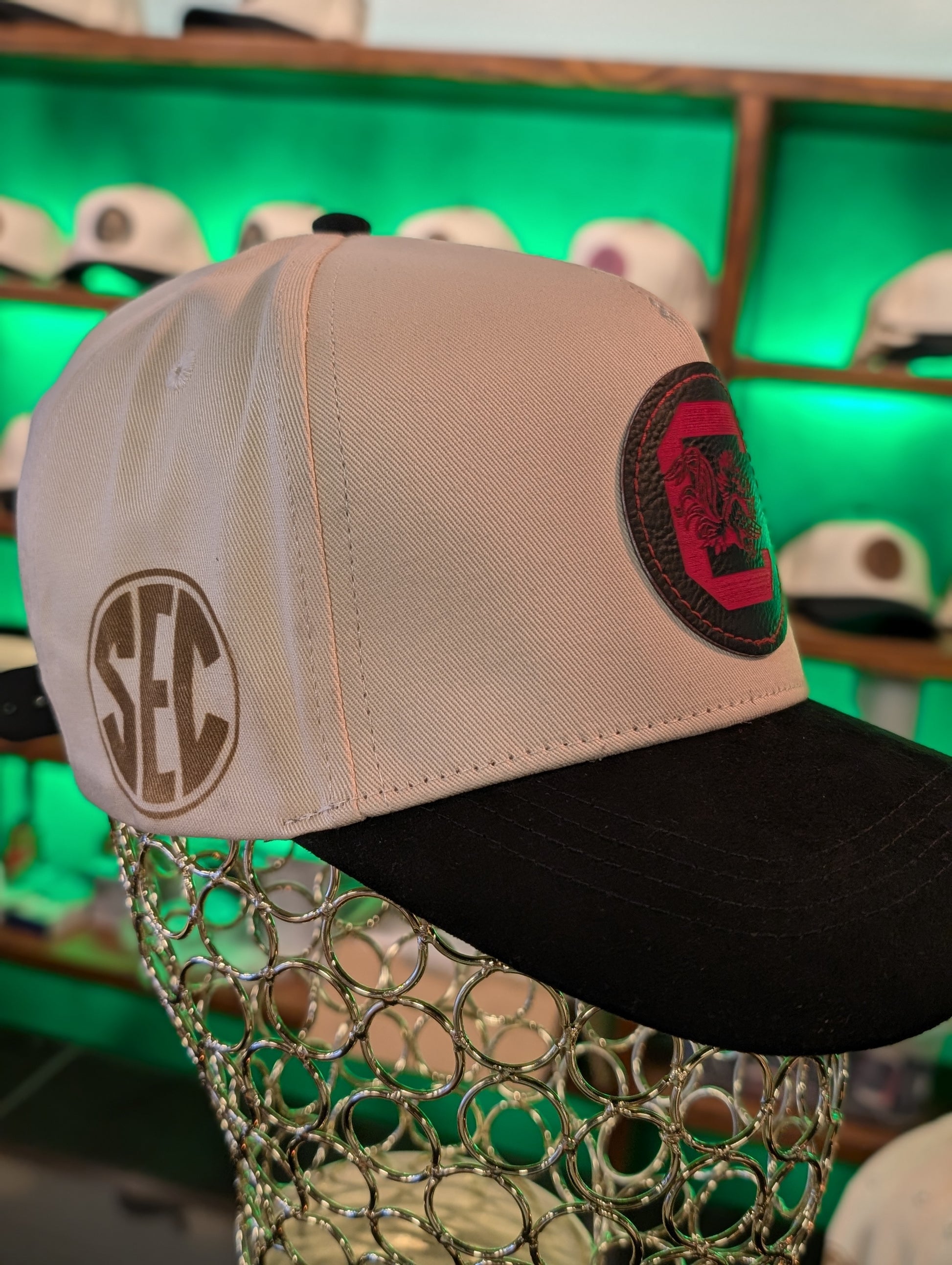 Beige and black cap with SEC logo on a mannequin head against a green background