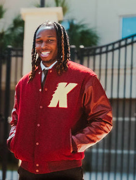 Person wearing a red letterman jacket with a large 'K' on a blurred outdoor background