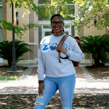 Person wearing a light blue sweatshirt with a logo and ripped jeans, standing outdoors.